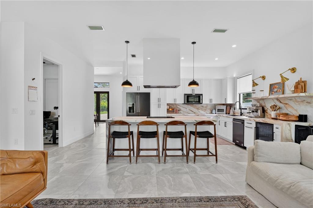 Open-concept kitchen featuring an oversized island, pendant lighting, marble-patterned countertops, white cabinetry, and stainless steel appliances