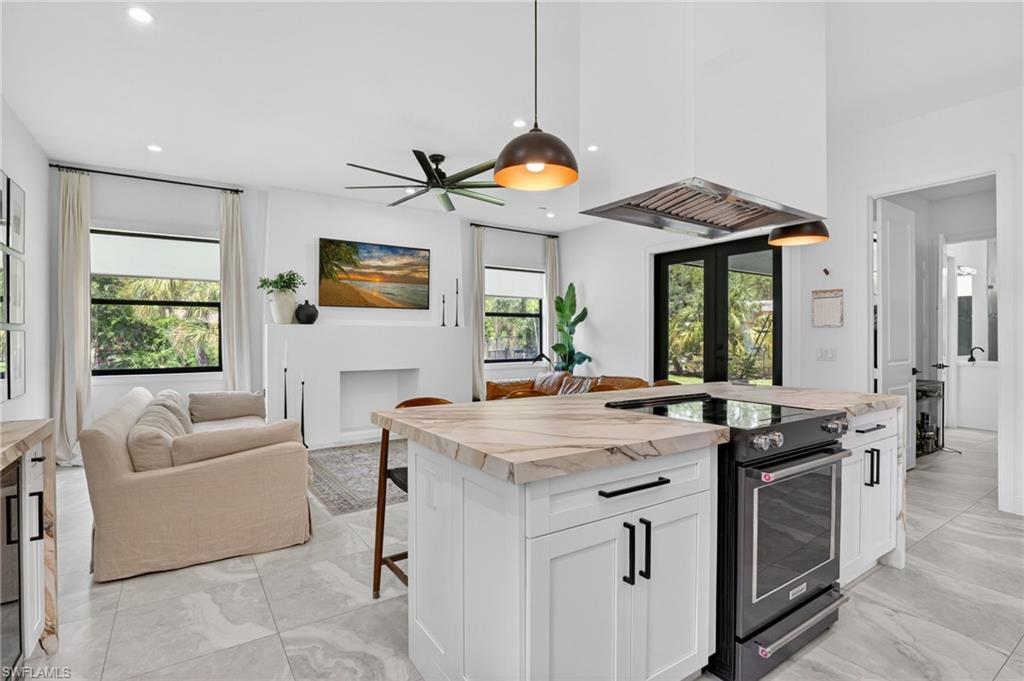 Open-concept living space featuring a kitchen island with integrated range, suspended range hood, and pendant lighting