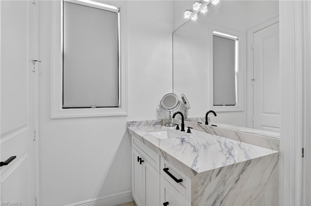 Bathroom vanity featuring a marbled countertop, integrated sinks, white cabinetry, and matte black hardware