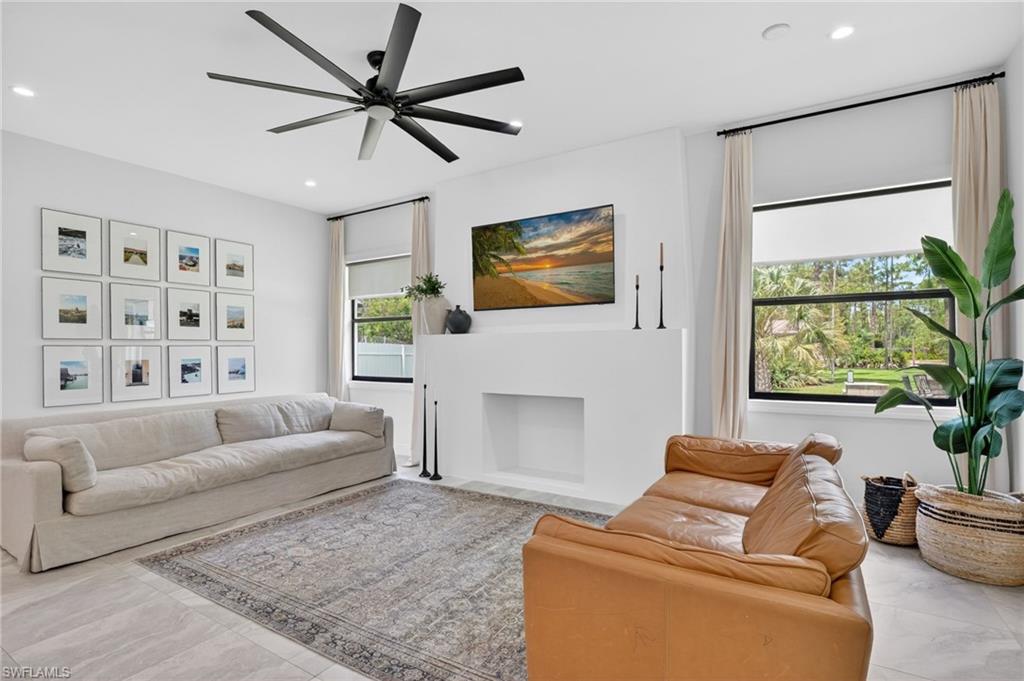 Spacious living area featuring large windows with verdant outdoor scenery, a contemporary fireplace, and light-toned tile flooring