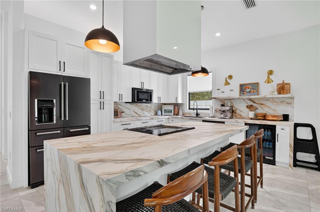 Gourmet kitchen featuring a waterfall island with stone countertop, white cabinetry, integrated black appliances, and a built-in beverage cooler