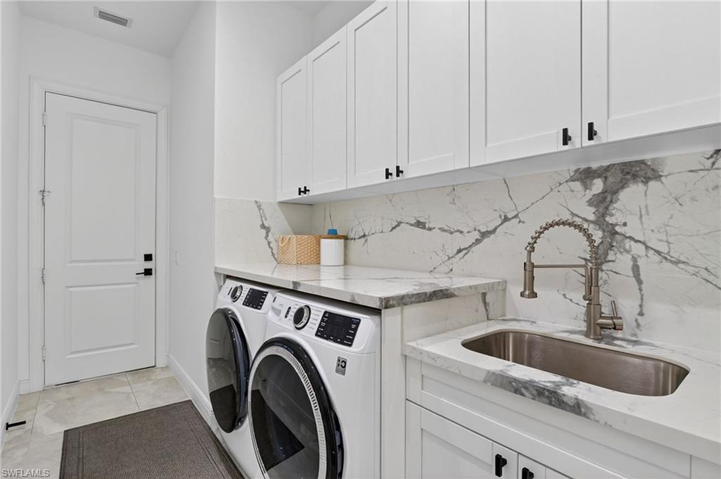 Laundry space featuring white shaker-style cabinetry with matte black hardware, a stainless steel sink with a pull-down faucet, and marble-look countertops with a matching backsplash