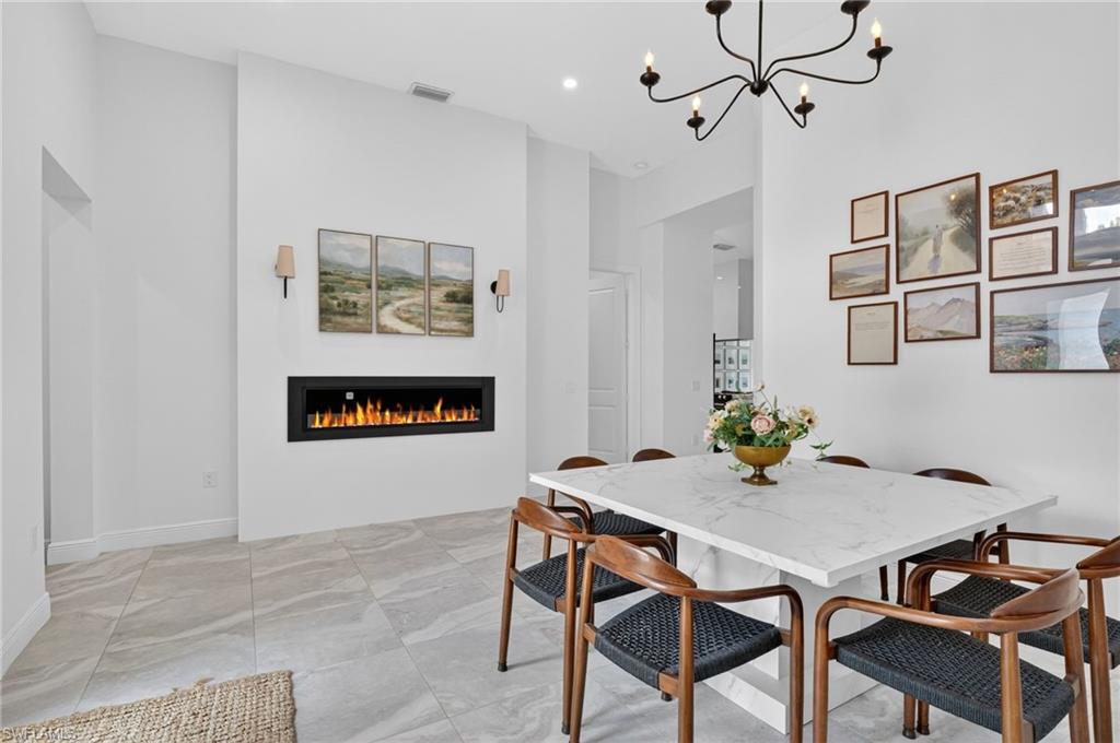 Recessed fireplace with a contemporary linear design, light tile flooring, white walls, and a multi-arm chandelier with candelabra bulbs