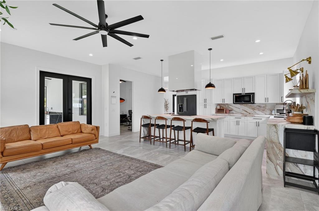 Open-concept living space featuring a gourmet kitchen with waterfall island, white cabinetry, and integrated appliances