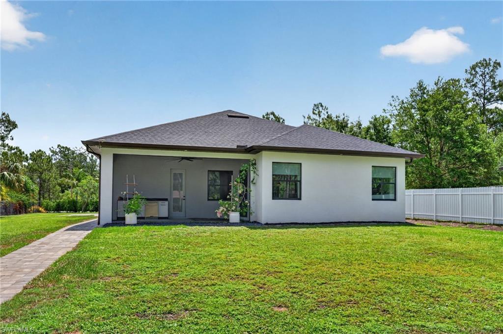 Rear exterior featuring a covered patio, dark shingle roof, white stucco siding, and a paved walkway