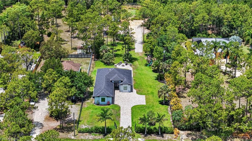 Aerial perspective showcasing a single-story residence with a dark shingle roof, surrounded by mature trees