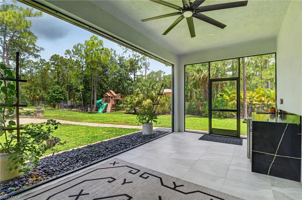 Covered patio featuring large format light-toned tile flooring, a black river rock bed, and a ceiling fan