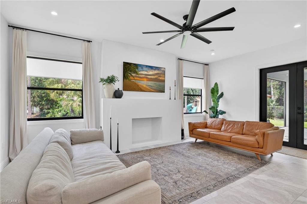 Spacious living area featuring light-toned flooring, a substantial built-in fireplace, and a contemporary ceiling fan