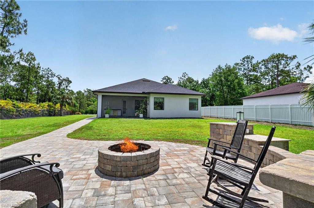 Expansive outdoor living area featuring a stone paver patio, built-in fire pit, and a stone seating wall