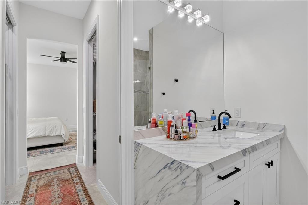 Dual sink vanity with a marble-finish countertop, matte black fixtures, and a spacious wall-mounted mirror with integrated lighting