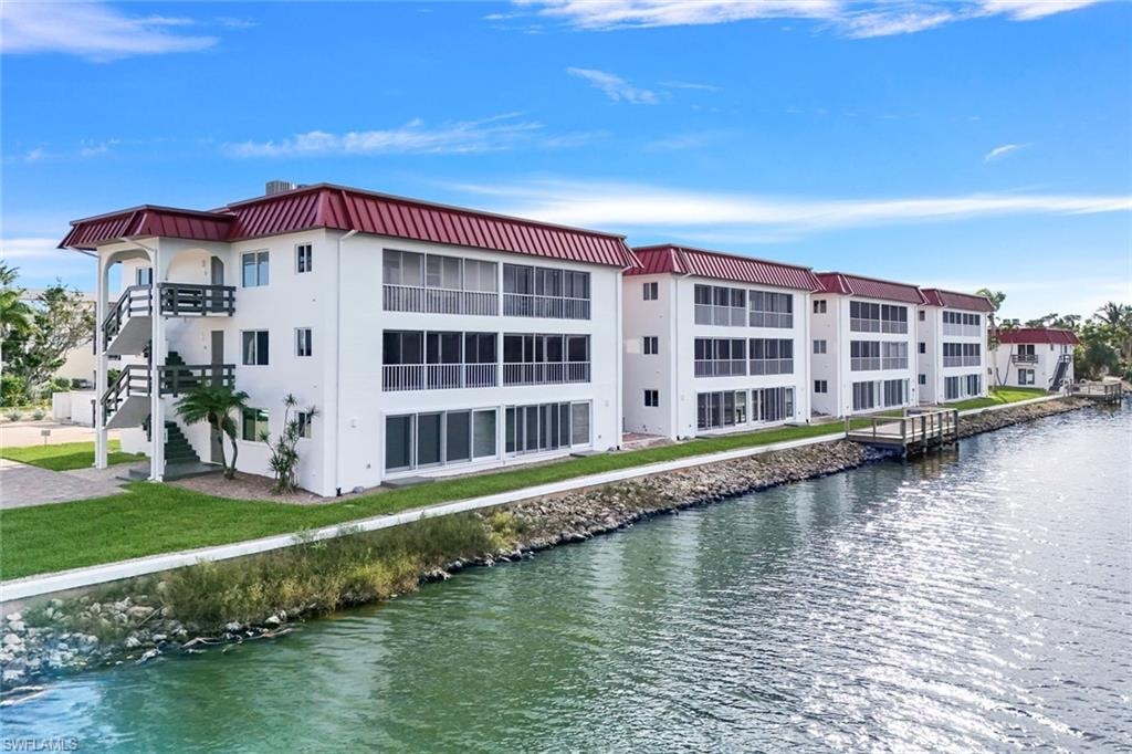 Waterfront condominium building featuring a red metal roof, white exterior, and multiple screened balconies