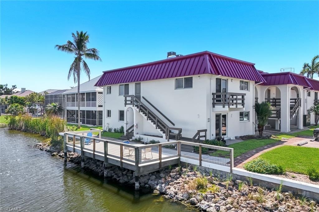 Waterfront property featuring a private wood dock with metal railings, white exterior, purple metal roof, and multiple balconies