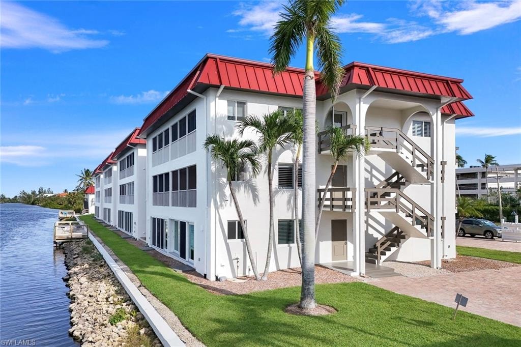 Waterfront condominium building featuring a red metal roof and white exterior