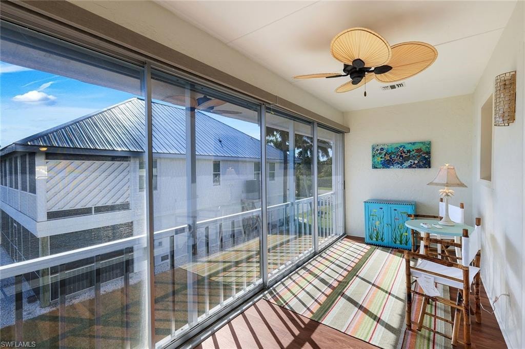 Enclosed patio featuring floor-to-ceiling sliding glass doors, wood-finish flooring, a ceiling fan, and white walls