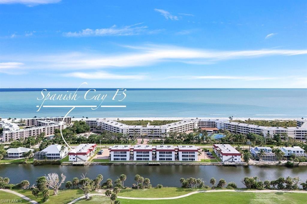 Waterfront condominium community with direct beach access, featuring multiple residential buildings, lush landscaping, and recreational amenities including a tennis court