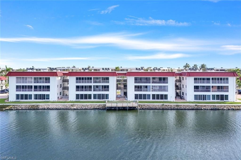 Waterfront building featuring red metal roofing, white exterior walls, multiple balconies with glass railings, and a private dock structure