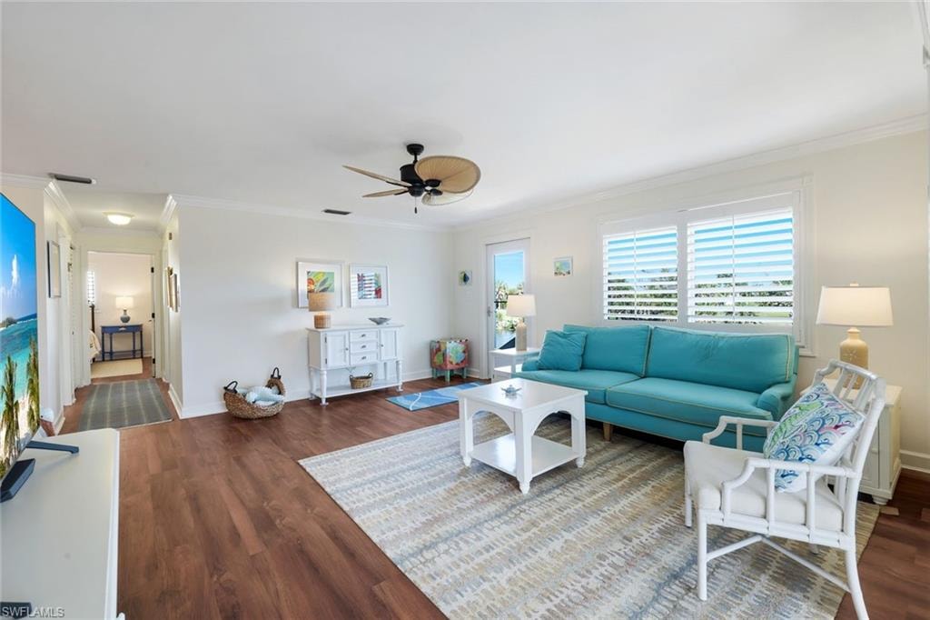 Spacious living area featuring wood-finish flooring, white plantation shutters, crown molding, and a ceiling fan with natural woven blades