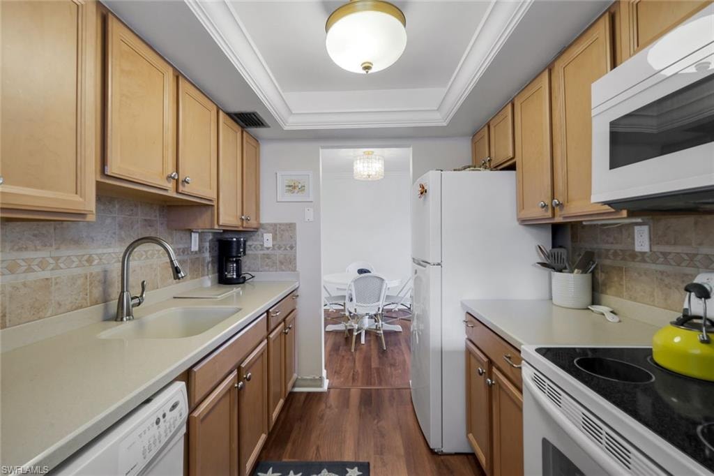 Galley kitchen featuring wood-finish cabinetry, light-toned countertops, a tiled backsplash, and stainless steel sink