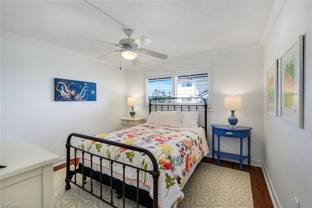 Hardwood-finish flooring featuring white baseboards, crown molding, a ceiling fan with integrated lighting, and a window with horizontal blinds