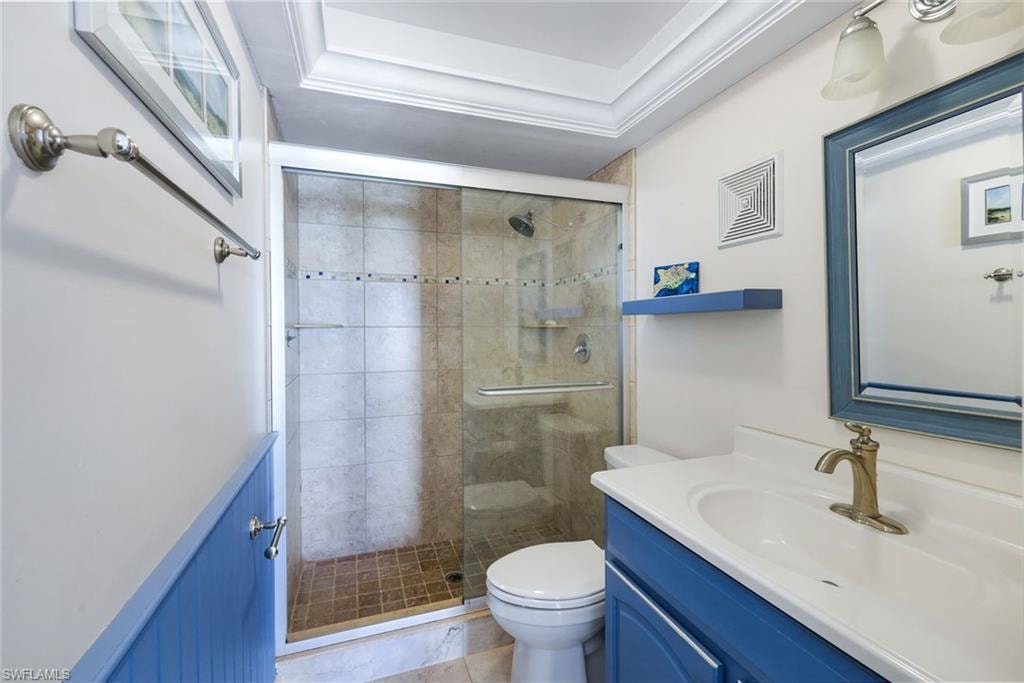Bathroom featuring a glass-enclosed shower with tile surround, a single vanity with a white countertop and brass-finish faucet, a framed mirror, and crown molding