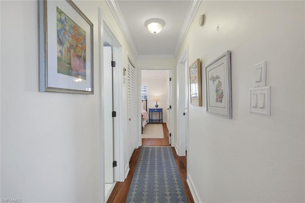 Hallway featuring wood-finish flooring, white trim, and crown molding