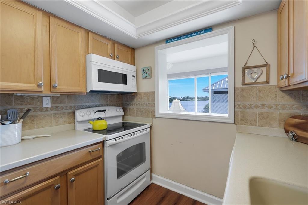 Kitchen featuring a pass-through window with water visible, wood-finish cabinetry, an over-the-range microwave, and a tile backsplash with decorative accents
