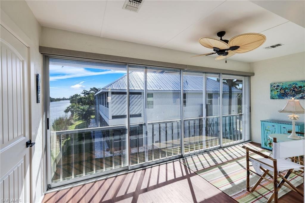Enclosed balcony with expansive water scenery, featuring large sliding glass panels, wood-finish flooring, and a ceiling fan with woven blades