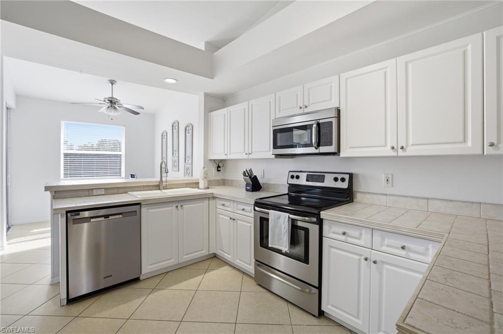 Kitchen with appliances with stainless steel finishes, white cabinets, a peninsula, light tile patterned flooring, and recessed lighting