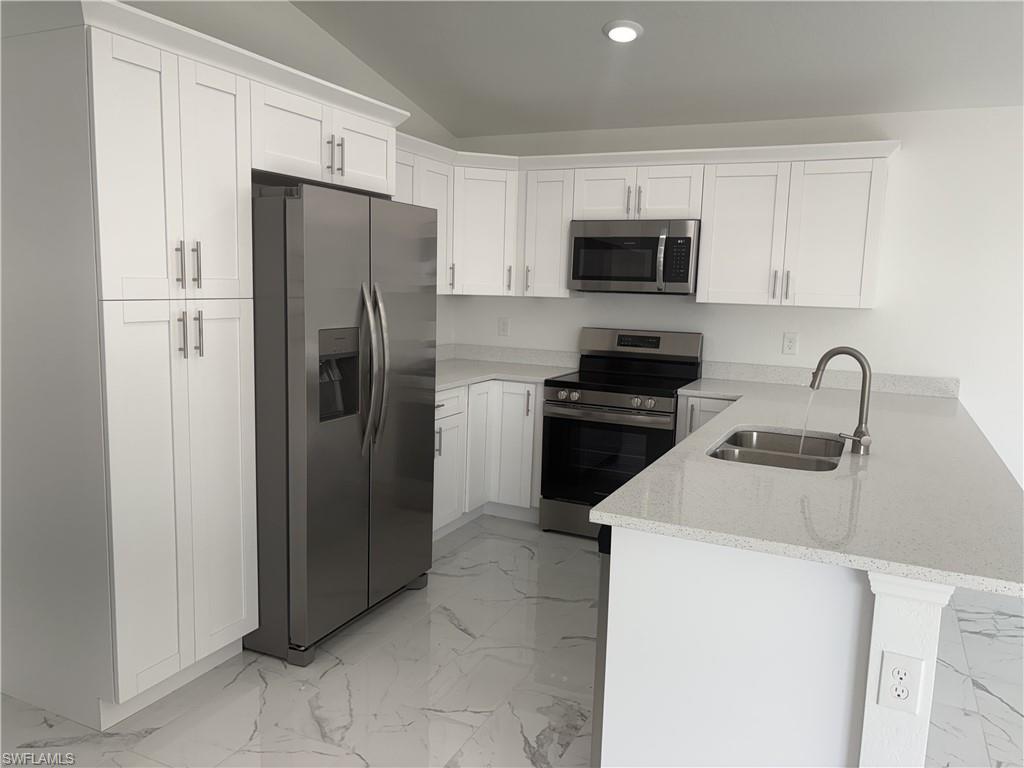 Modern kitchen featuring white shaker cabinetry, stainless steel appliances, light-toned countertops, a stainless steel undermount sink with a gooseneck faucet, and large format marble-look tile flooring