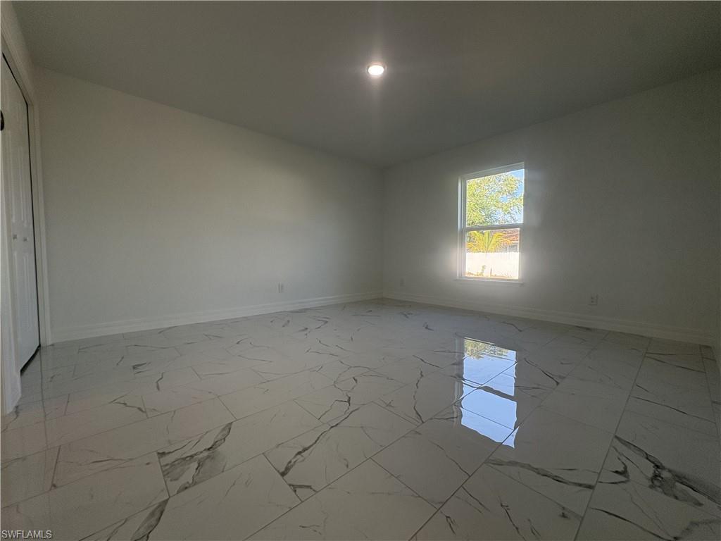 Spacious interior room featuring white walls, bright window, recessed lighting, white baseboards, and large format white tile flooring with grey veining