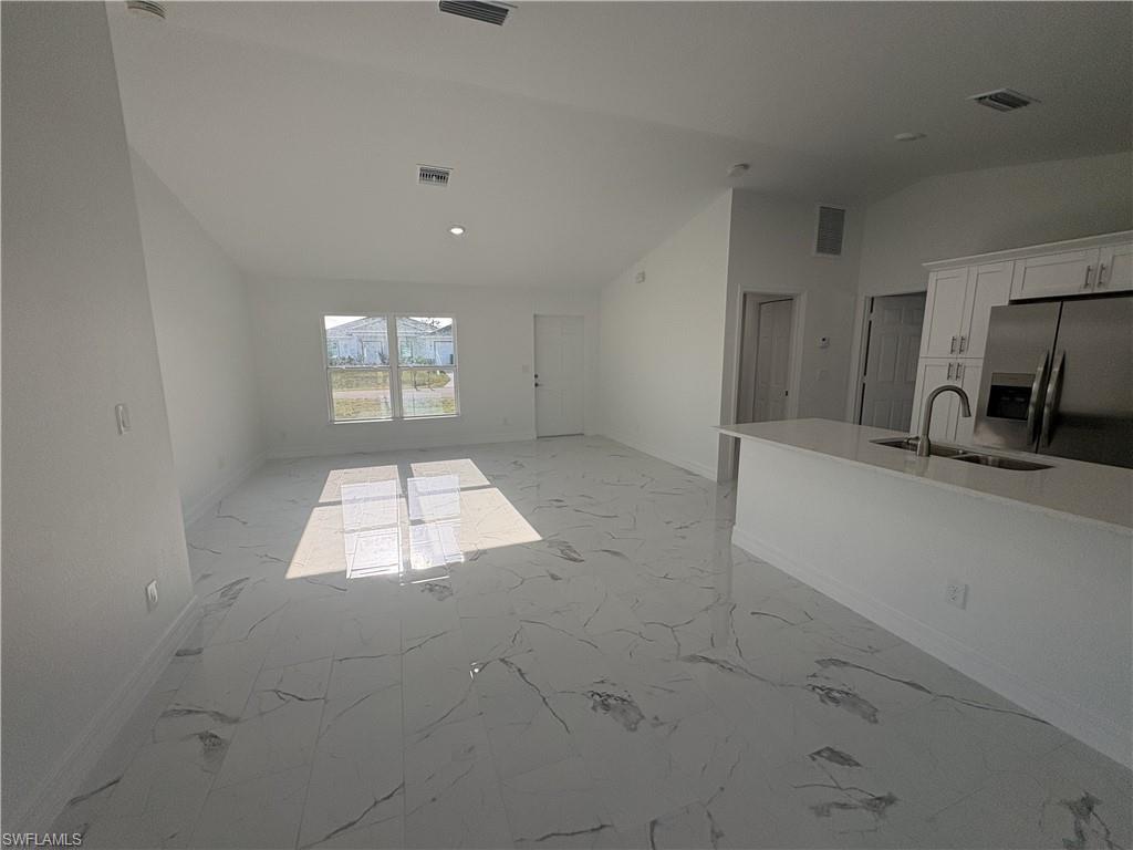 Open-concept living space featuring high vaulted ceilings, large windows, sleek tile flooring, a kitchen island with an undermount sink, and stainless steel appliances