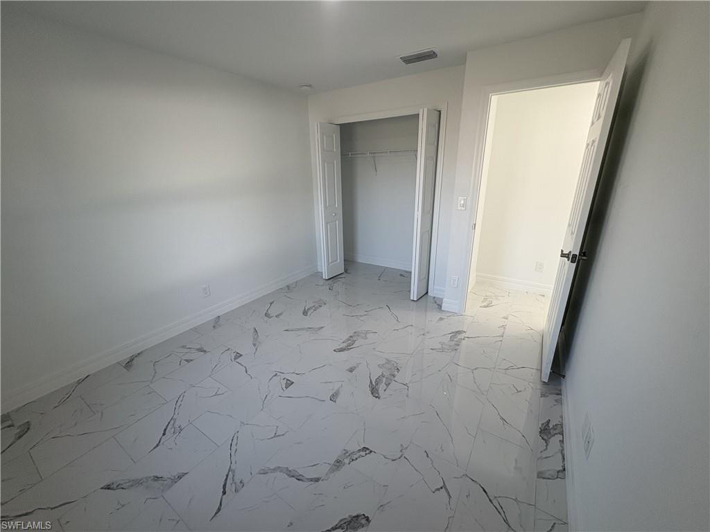 Spacious interior room featuring white walls, large format tile flooring with grey veining, and a built-in closet with bifold doors