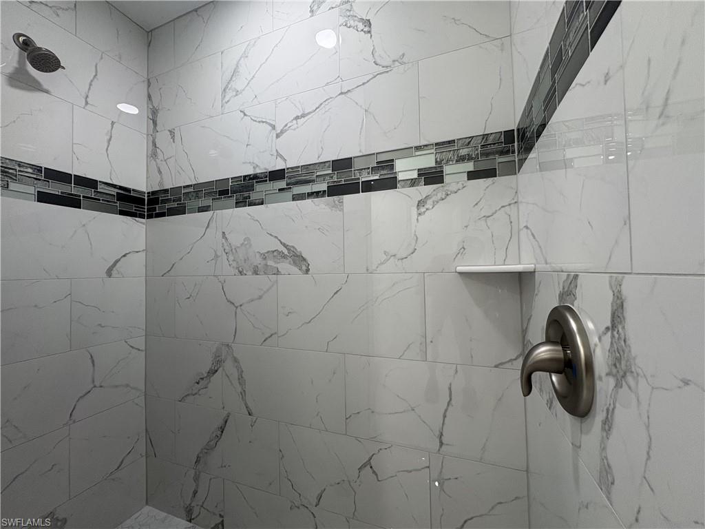 Tiled shower featuring large format white and grey marbled-look tiles, a decorative mosaic tile accent band, a built-in shelf, and brushed nickel fixtures