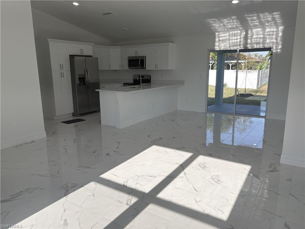 Spacious interior with white porcelain tile flooring and a modern kitchen featuring white cabinetry, stainless steel appliances, and a peninsula with a breakfast bar