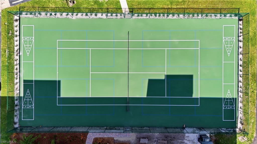 Multi-sport court featuring pickleball and tennis lines, integrated shuffleboard courts, black chain-link fencing, and surrounding green space - Virtually Edited Image