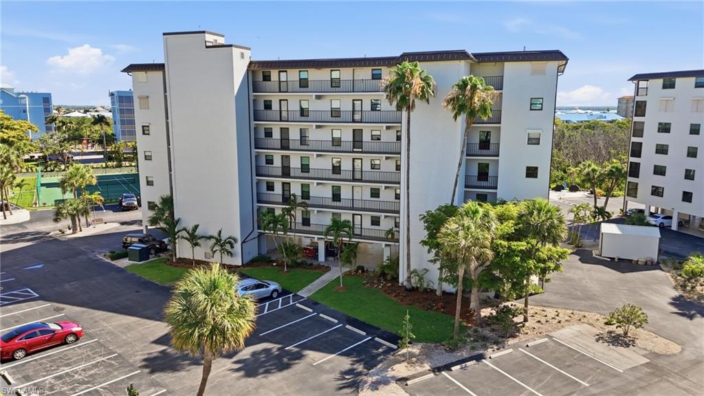 Modern multi-story building featuring individual balconies, a large parking area, and mature palm trees - Virtually Edited Image