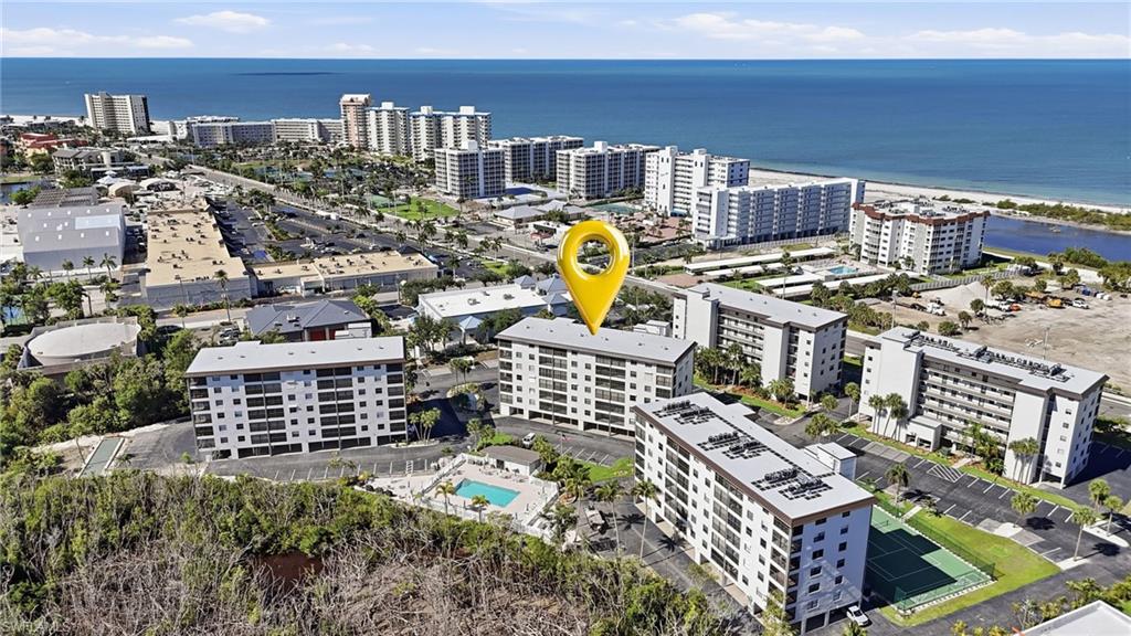Coastal community featuring multiple multi-story residential buildings, ample surface parking, recreational pool, and tennis courts - Virtually Edited Image