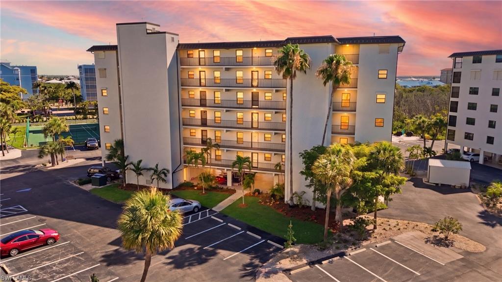Multi-story building featuring multiple private balconies, exterior lighting, mature palm trees, and a paved parking area - Virtually Edited Image