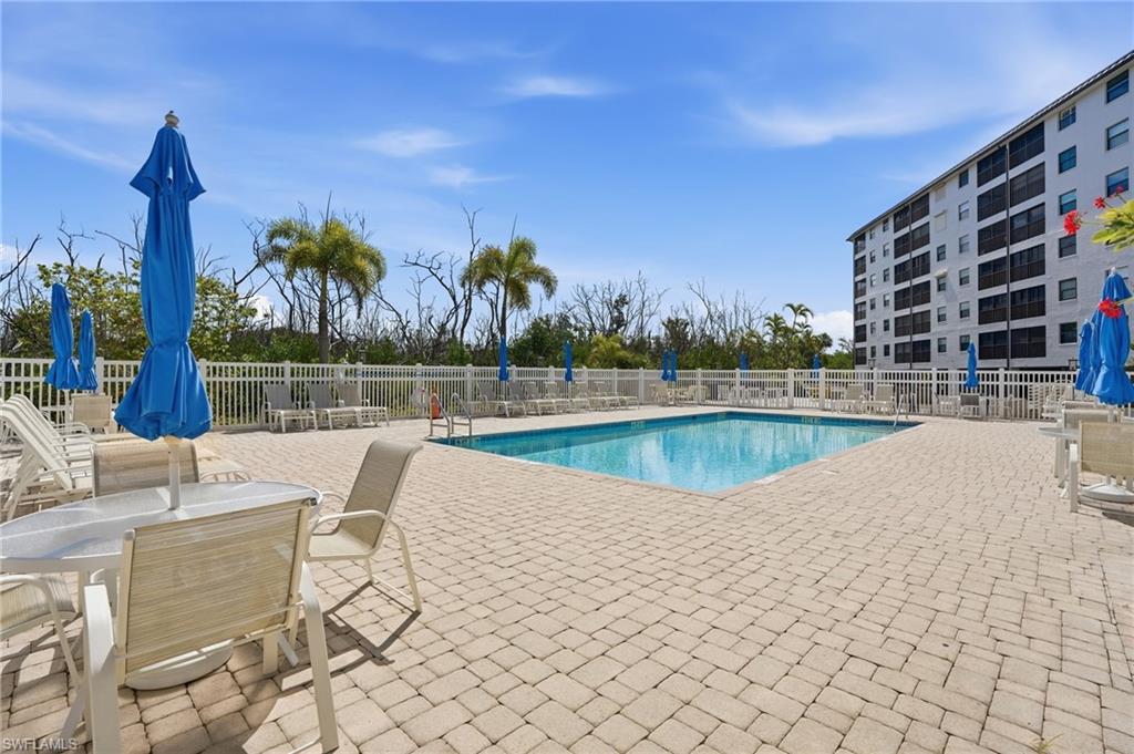 Outdoor swimming pool surrounded by a paver deck, white perimeter fencing, and established palm trees - Virtually Edited Image