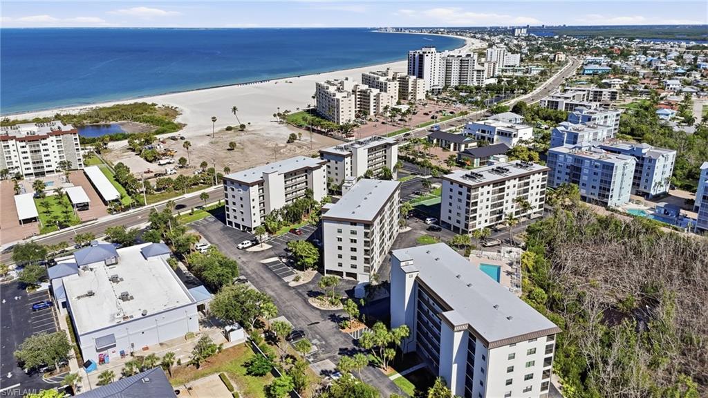 Coastal community featuring multiple mid-rise residential buildings, a visible swimming pool, and proximity to a wide sandy beach - Virtually Edited Image
