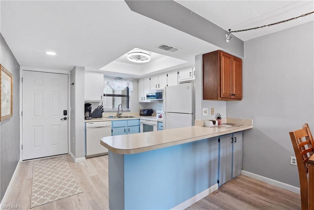 Kitchen featuring light wood-finish flooring, white appliances, and a breakfast bar - Virtually Edited Image