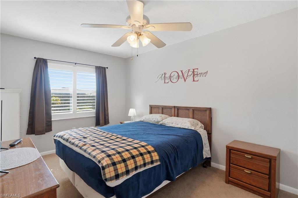Bedroom featuring a ceiling fan with light fixture, plantation shutters, and carpeted flooring