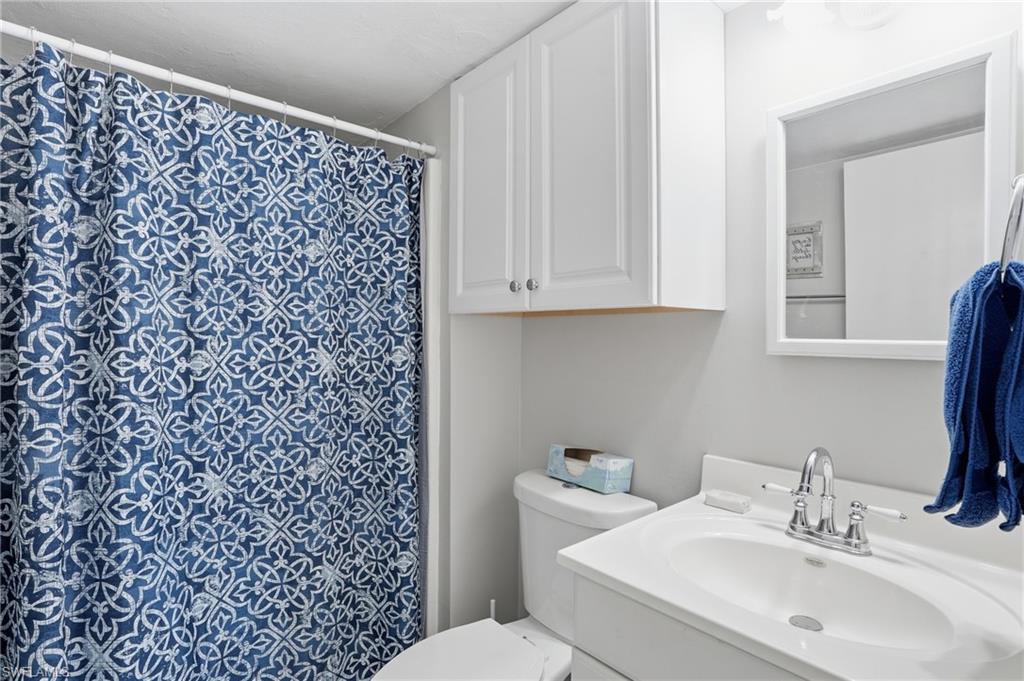 Primary Bathroom featuring a white vanity with integrated sink, chrome faucet, wall-mounted mirror, and white overhead cabinetry - Virtually Edited Image