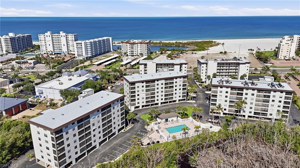 Aerial view of multiple multi-story residential buildings featuring balconies, a swimming pool with surrounding patio, and palm trees - Virtually Edited Image