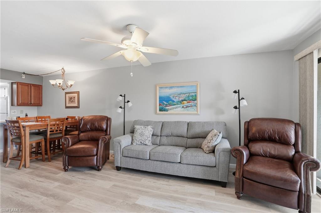 Open-concept living space featuring wood-finish flooring, a ceiling fan with integrated lighting, and light gray wall paint - Virtually Edited Image