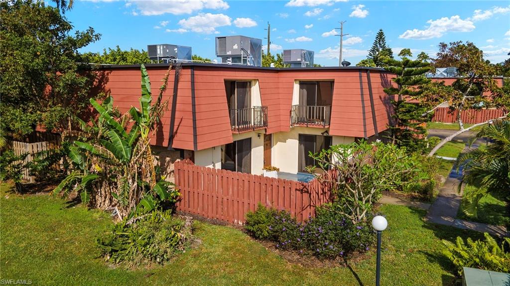 Multi-level exterior featuring a red mansard roof, two private balconies with iron railings, and a red wood fence