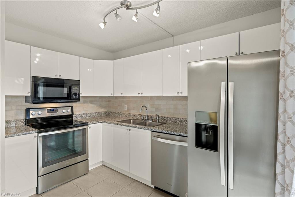 Modern kitchen featuring high-gloss white cabinetry, stainless steel appliances, granite countertops, a tiled backsplash, and recessed lighting