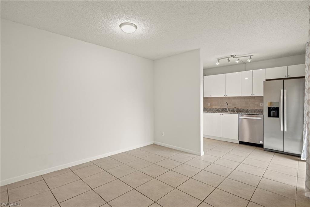 Neutral-toned tile flooring extends into a kitchen featuring white flat-panel cabinetry, stainless steel appliances, and track lighting