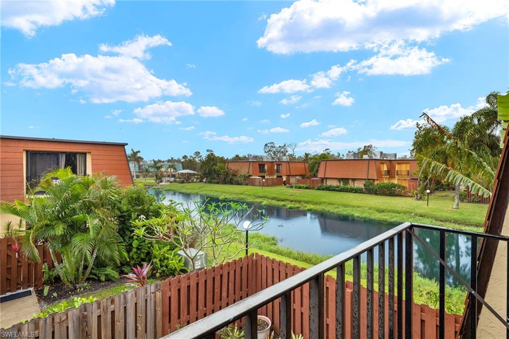 Balcony overlooking a tranquil body of water, bordered by a manicured grassy bank and tropical landscaping