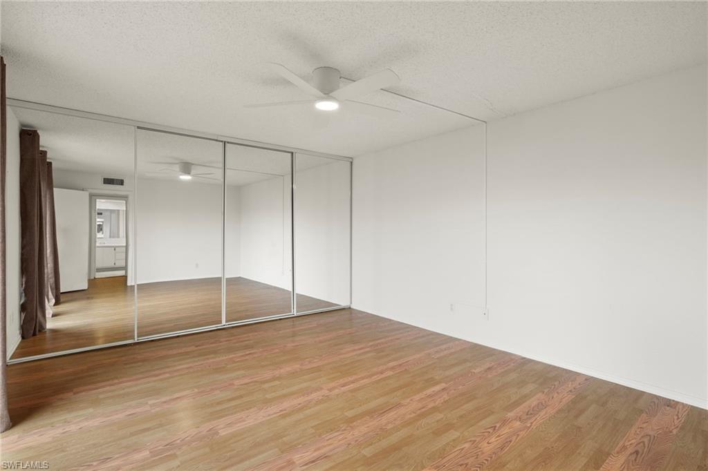 Spacious room featuring wood-finish flooring, a contemporary ceiling fan with integrated lighting, and a wall of mirrored closet doors
